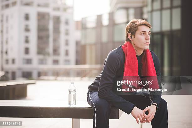 young male runner taking a break on bench in city square - headphone man on neck stock pictures, royalty-free photos & images