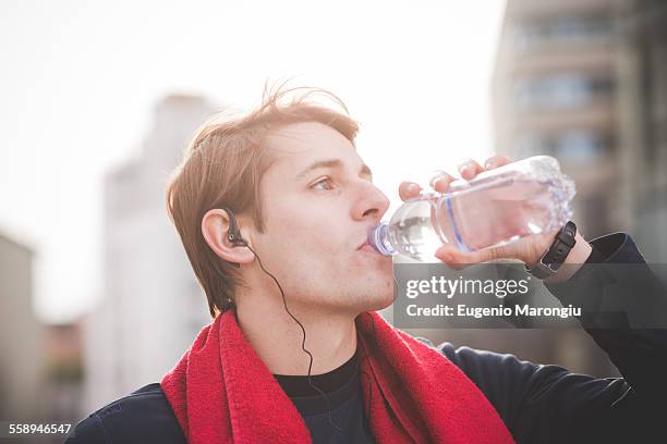 young male runner drinking water - headphone man on neck stockfoto's en -beelden