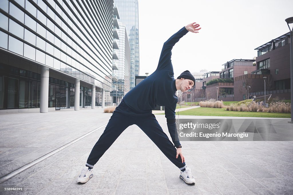 Young male runner stretching in city