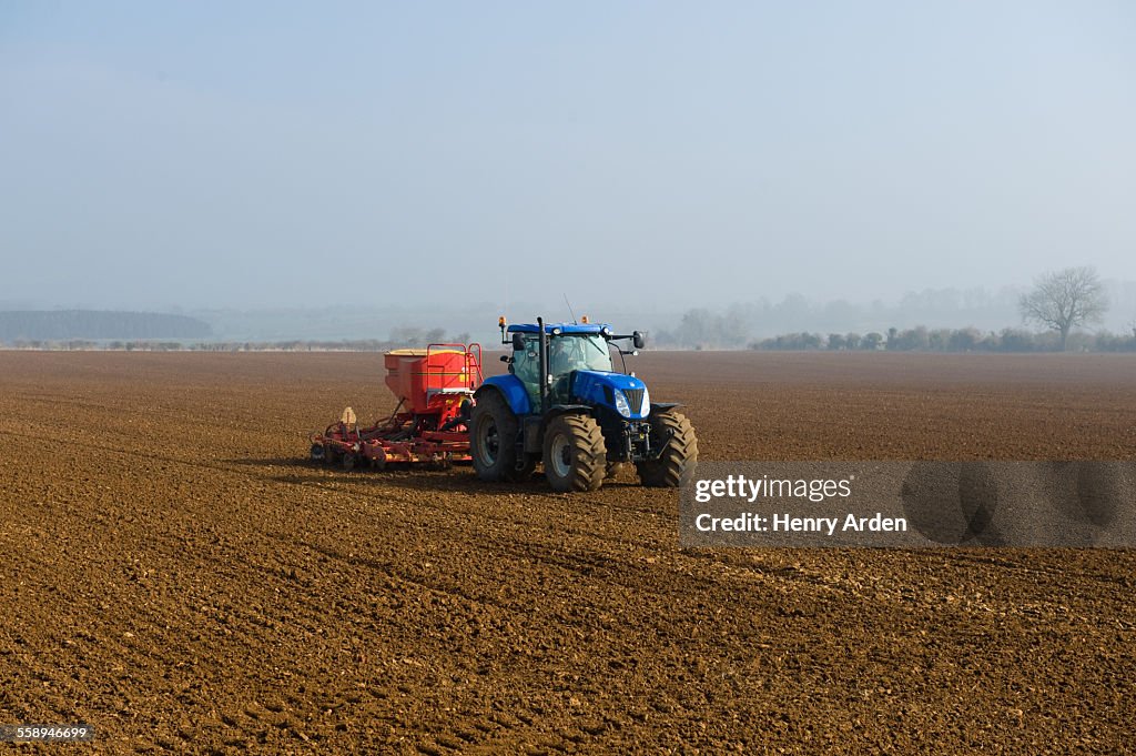 Tractor drilling seed in ploughed field on misty morning