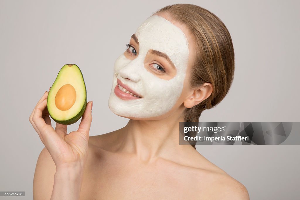 Portrait of young woman wearing face mask, holding avocado