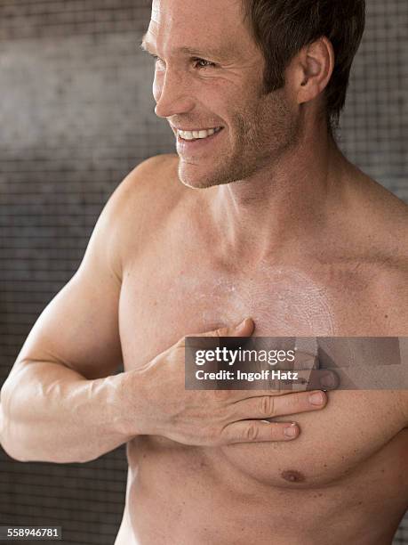 bare chested muscular man in bathroom rubbing moisturizer on chest - chest torso stockfoto's en -beelden