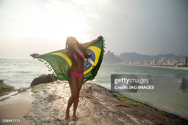 young woman holding up brazilian flag, ipanema beach, rio de janeiro, brazil - ipanema beach stock pictures, royalty-free photos & images