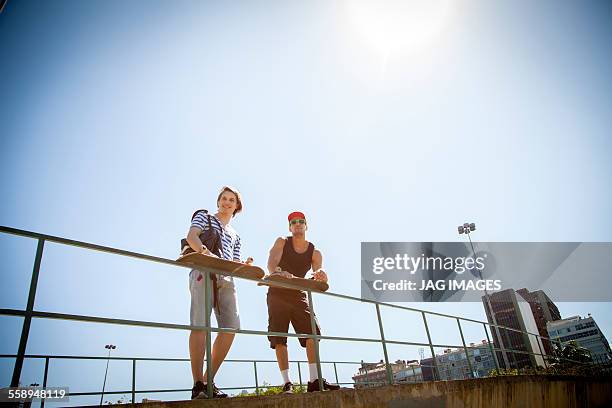 two men, holding skateboards, leaning on railings, low angle view - baranda fotografías e imágenes de stock