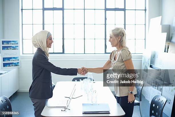 young businesswoman and mature businesswoman shaking hands in office - reglas de sociedad fotografías e imágenes de stock