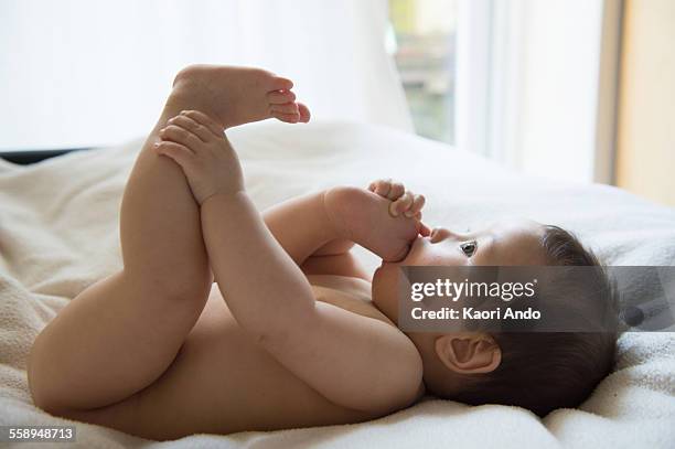 baby boy lying on back with toes in mouth - teen stockfoto's en -beelden