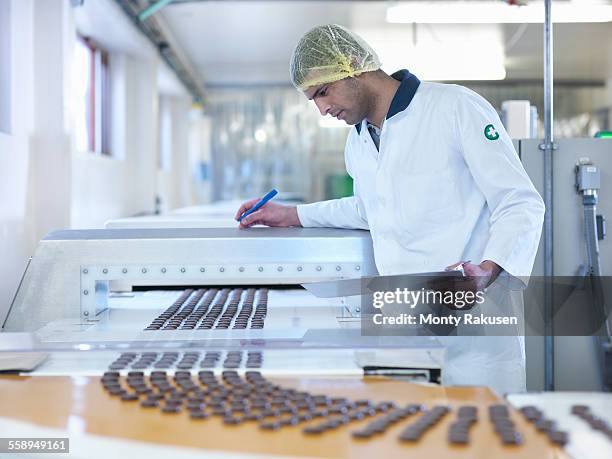 worker inspecting chocolate on production line in chocolate factory - chocolate factory stock-fotos und bilder