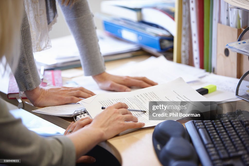 Cropped shot of two businesswomen checking paperwork at office desk
