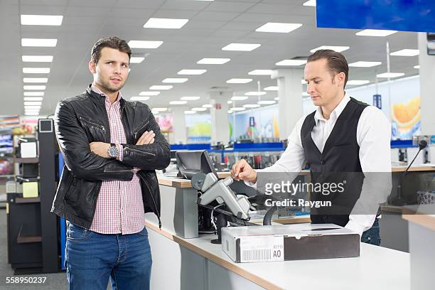 unsure shopper paying with credit card in electronics store - excess product stock pictures, royalty-free photos & images