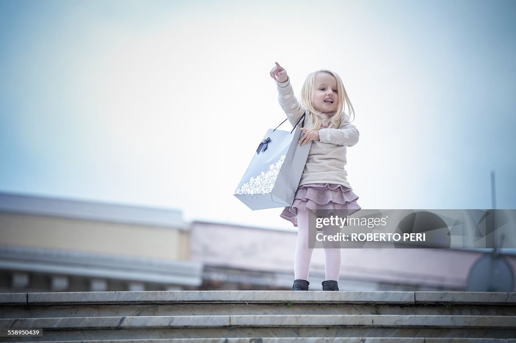 Young girl pointing from stairway carrying shopping bag, Cagliari, Sardinia, Italy
