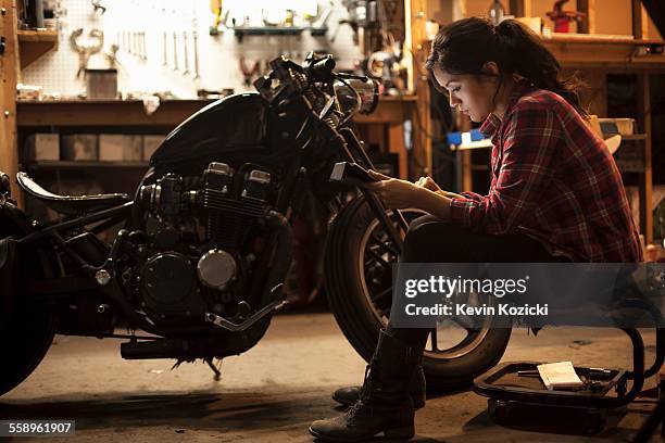 female mechanic working on motorcycle in workshop - motorcycle mechanic stock pictures, royalty-free photos & images