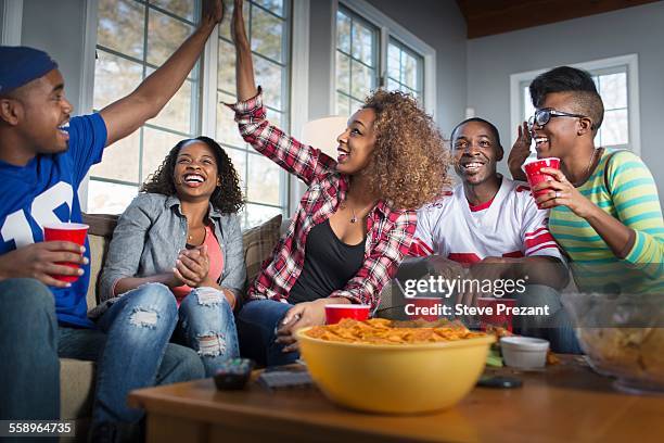 five adult friends celebrating with high five whilst watching tv from sofa - black man high 5 stockfoto's en -beelden