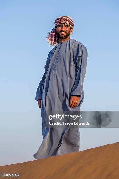 a muslim man standing on a sand dune at sunset wearing a traditional dishdasha and masar. - dishdasha stockfoto's en -beelden