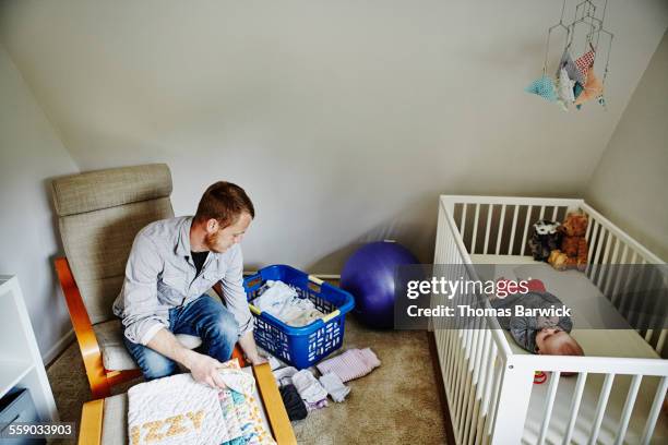 Father folding laundry while baby lies in crib