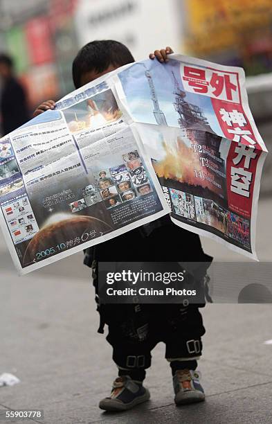 Chinese young boy reads a special edition of local newspaper featuring the launch of Shenzhou VI spacecraft at a street on October 12, 2005 in...