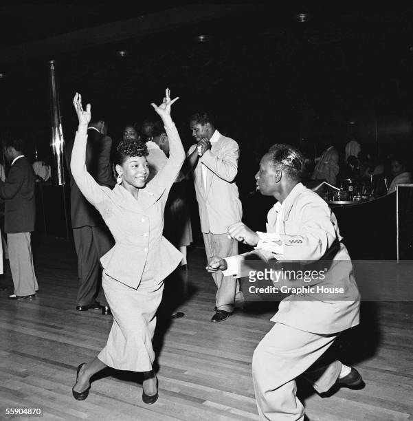 Woman throws her arms in the air as she swing dances with a man at the Savoy Ballroom, Harlem, New York, late 1940s.