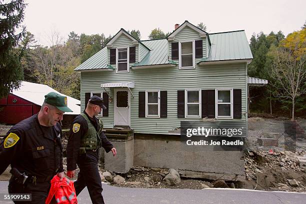 New Hampshire state police troopers walk past a house, where all the ground around it was washed away exposing its foundation, along Route 123...