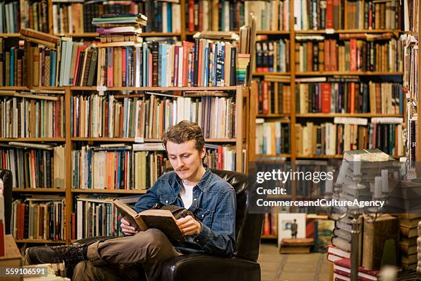 young man reading in second hand bookstore - bookstore stock-fotos und bilder