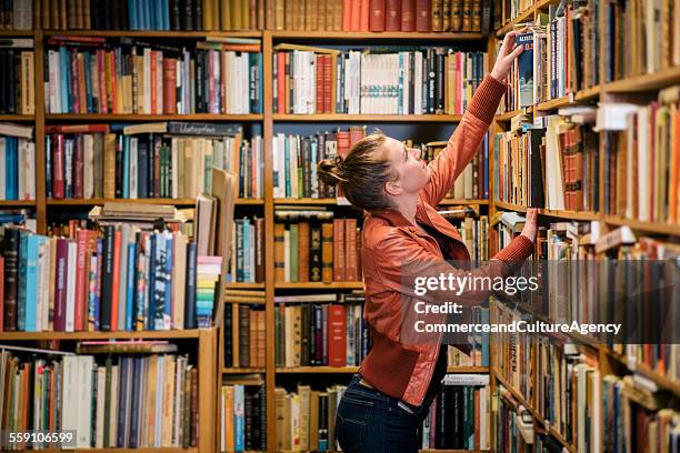 young woman reading in second hand bookstore - kringloopwinkel stockfoto's en -beelden
