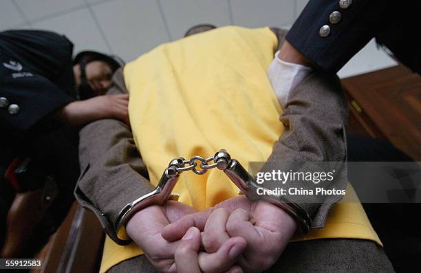 Policemen escort a handcuffed gang member during a trial at the Meishan Intermediate People's Court on October 12, 2005 in Meishan of Sichuan...