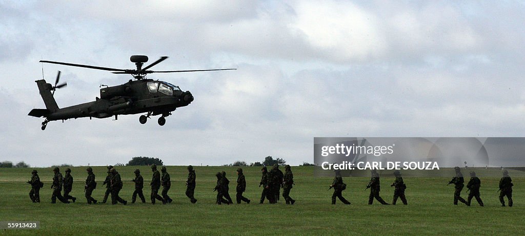 An Apache helicopter flies past soldiers