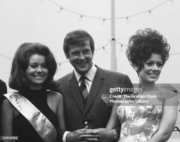 English actor Roger Moore with two beauty queens at a Variety Club of Great Britain event, circa 1970.