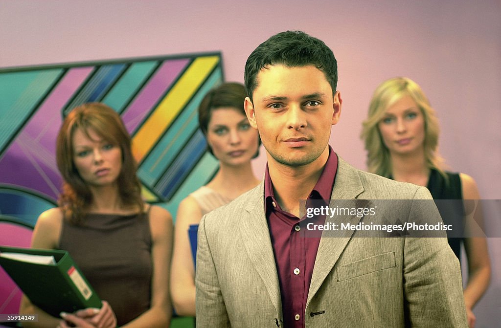 Portrait of a businessman with three businesswomen standing behind him in an office