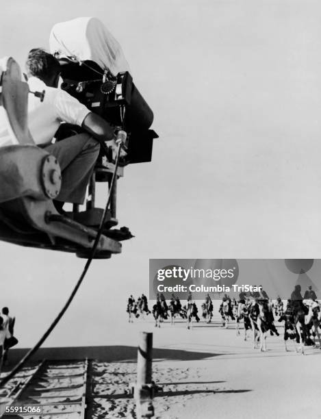 Cameraman on a crane films a shot of actors approaching on camels in a scene from the film 'Lawrence of Arabia,' directed by David Lean, 1962.