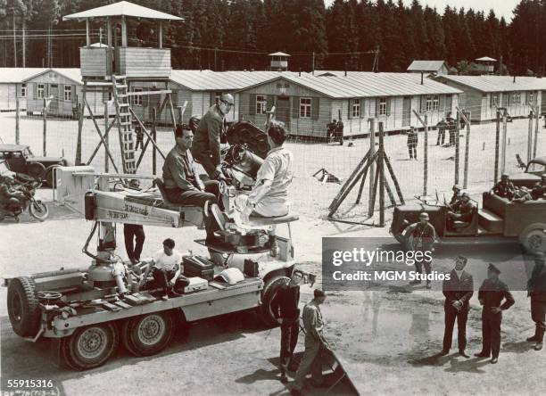 Camera crew, including American director John Sturges sits on a mobile crane just outside the wire fence of a prisoner of war camp on the set of the...