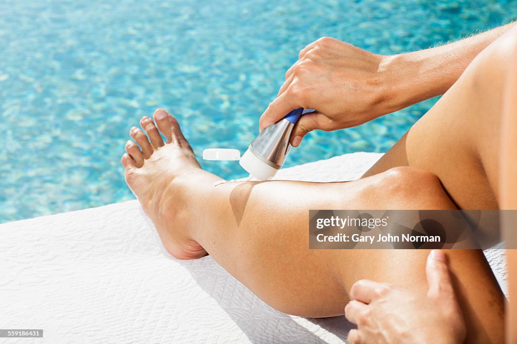 Woman putting sun cream on her legs, close up.