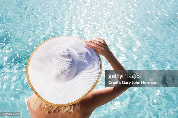 young woman sitting by pool wearing hat, rear view - sun hat stock pictures, royalty-free photos & images