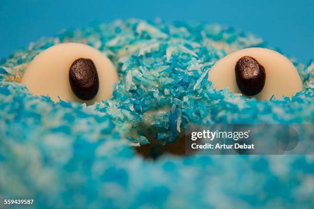 Blue donut covered with coconut with two eyes of chocolate and blue background.