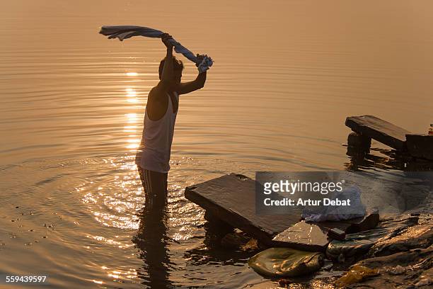 Man washing his laundry on the Ganges shoreline during the sunrise in Varanasi. India, Asia.