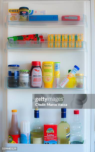 Well kept organized and clean shelves of fridge containing dressing, sauces, white wine, milk soy sauce, vitamins olives and bw films
