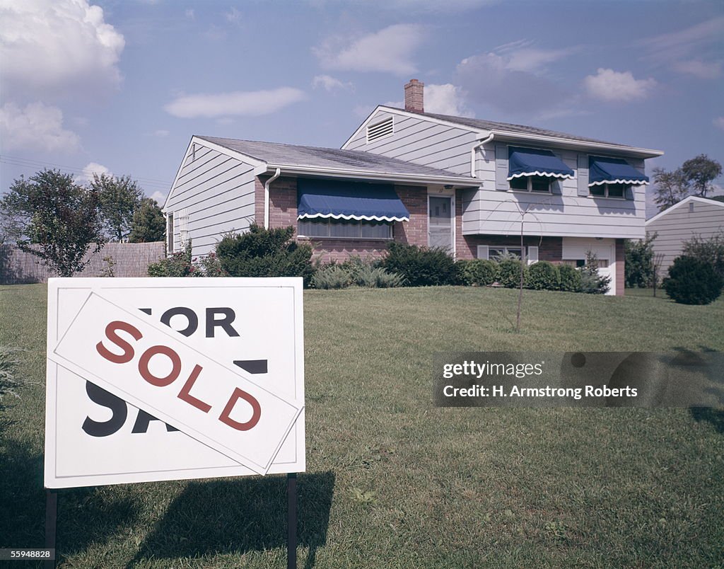 Suburban House With Blue Awnings And A Sold Sign O