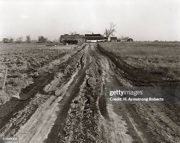 Circa 1940s: Dirt Road Leading Up To Old Farm House Surrounded By Barn & Sheds.