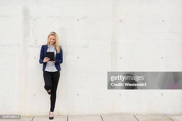 smiling businesswoman with digital tablet leaning on concrete wall - bien vestido fotografías e imágenes de stock