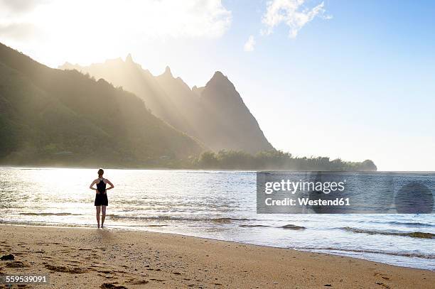 usa, hawaii, hanalei, woman standing on haena beach, view to na pali coast in the evening light - hanalei stock pictures, royalty-free photos & images