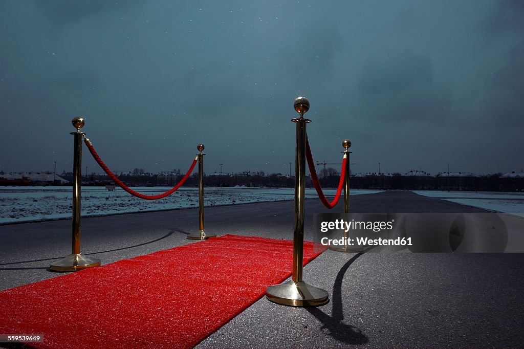 Red carpet on street, city in the background, dark clouds