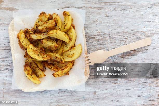 baked potato wedges with herbs and parmesan on greaseproof paper and wooden plate - cheese wedge foto e immagini stock