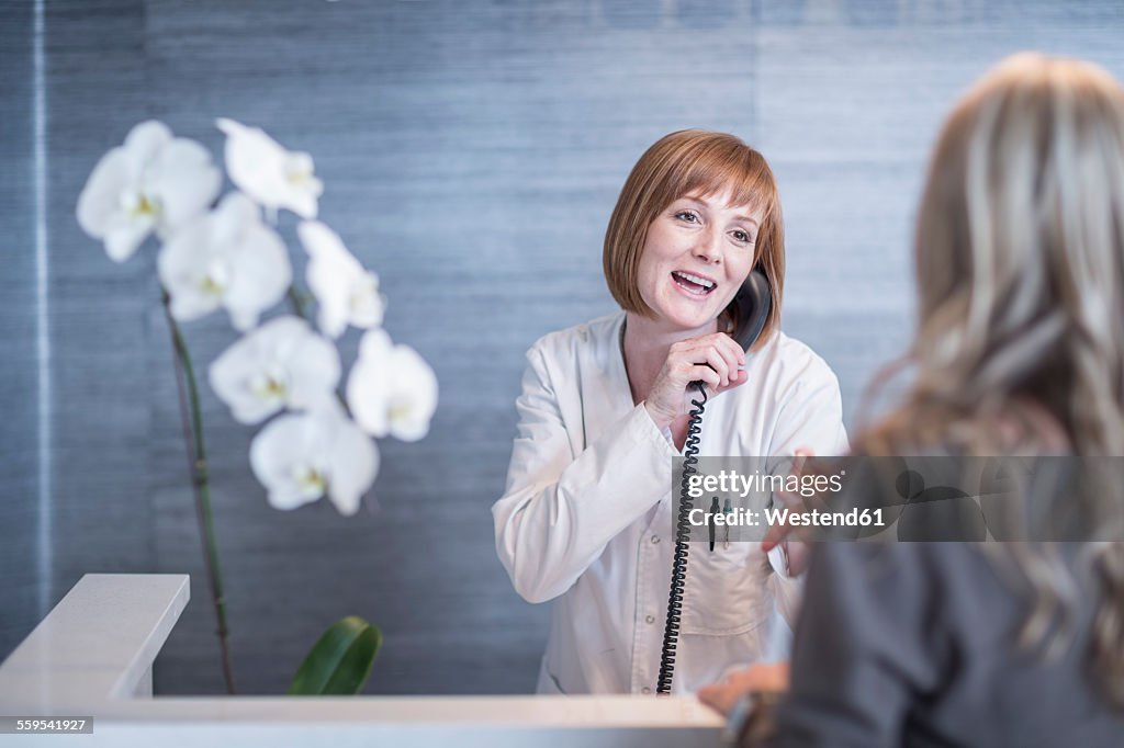 Receptionist greeting patient while on the phone