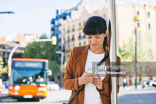 spain, barcelona, businesswoman with smartphone waiting at the bus stop - busstop stock-fotos und bilder
