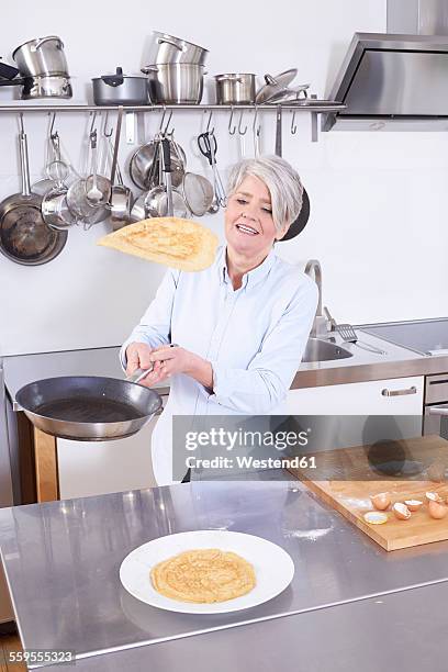 mature woman in kitchen throwing up pancake in pan - pancake toss stock-fotos und bilder