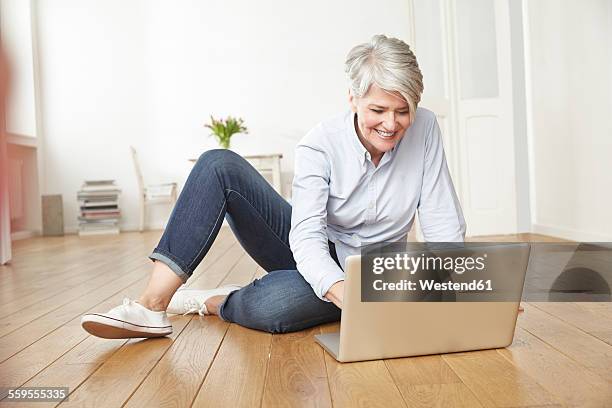 mature woman sitting on floor using laptop - einzelne frau über 40 stock-fotos und bilder