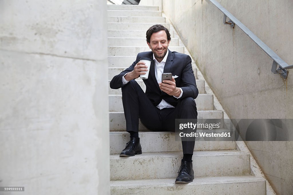 Businessman with coffee to go using smartphone in a modern building