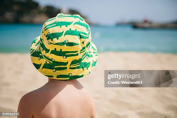 spain, mallorca, porto christo, back view of little boy sitting on the beach wearing summer hat - back detail stock pictures, royalty-free photos & images