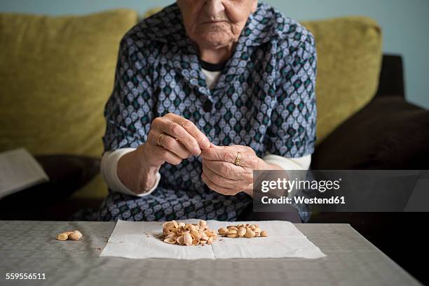 aged woman eating pistachios at home - banknoten stockfoto's en -beelden