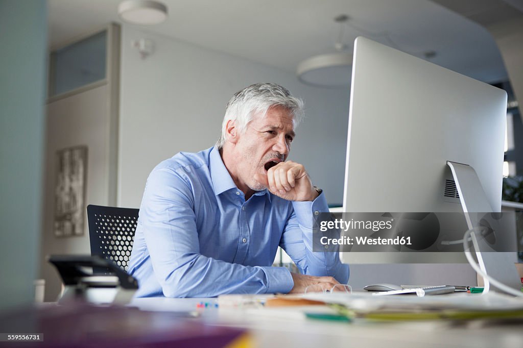 Businessman sitting at desk, yawning