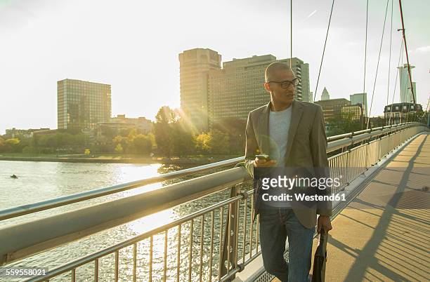 germany, frankfurt, businessman walking on bridge - main smartphone stockfoto's en -beelden