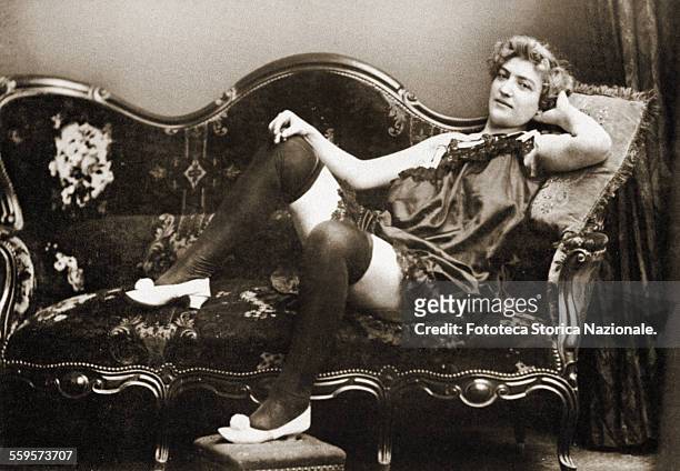 Portrait of a transgender woman lying in seductive pose on the sofa, dressed with only underwear. Italy approx. 1900 .